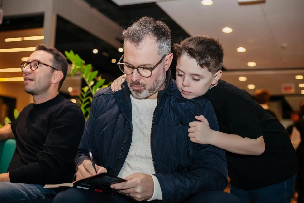 O pai do Enrico autografa o livro Curva Zero enquanto Enrico o abraça por trás
