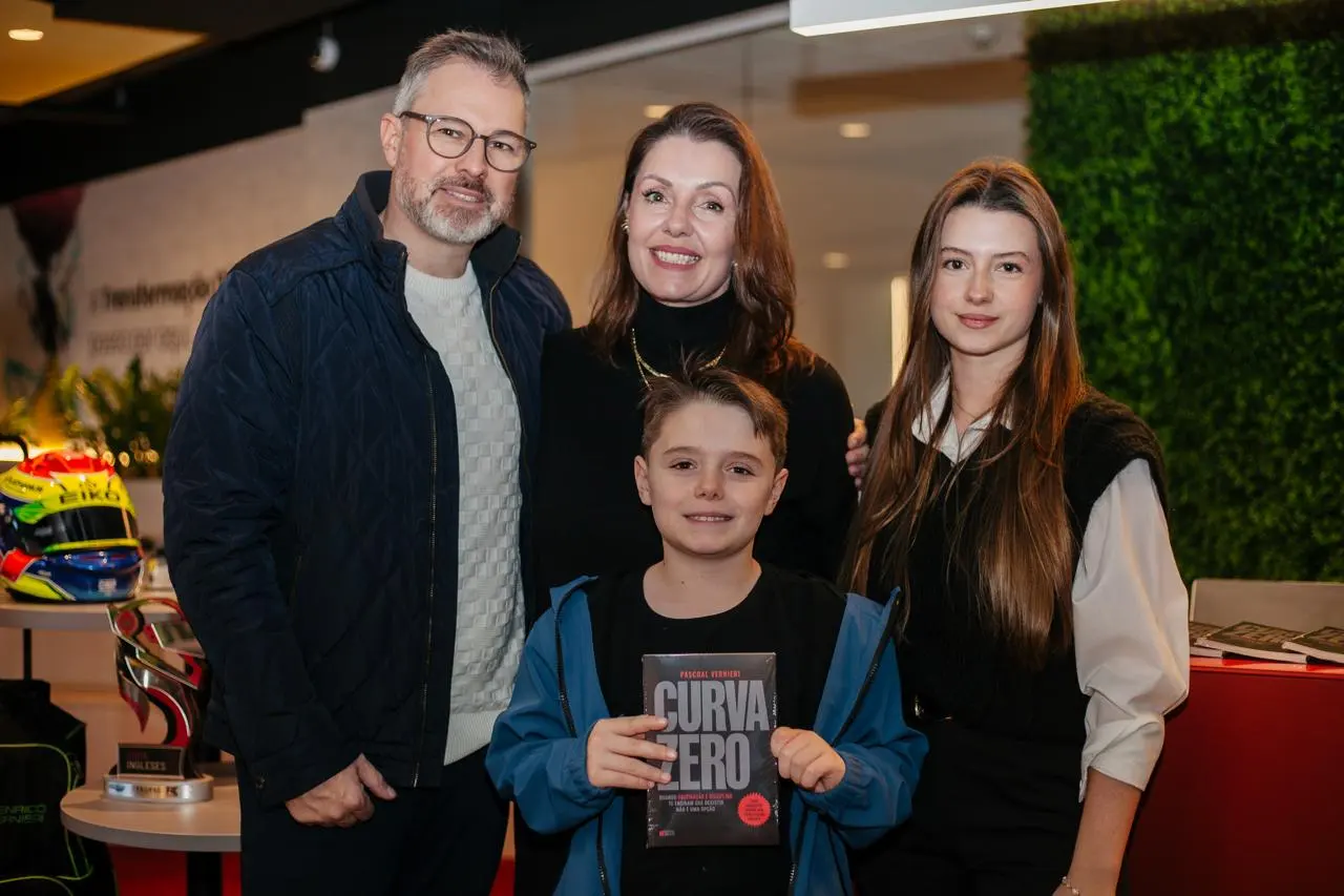 Enrico segura o livro Curva Zero, cercado pela família, em frente ao capacete e ao troféu de kart