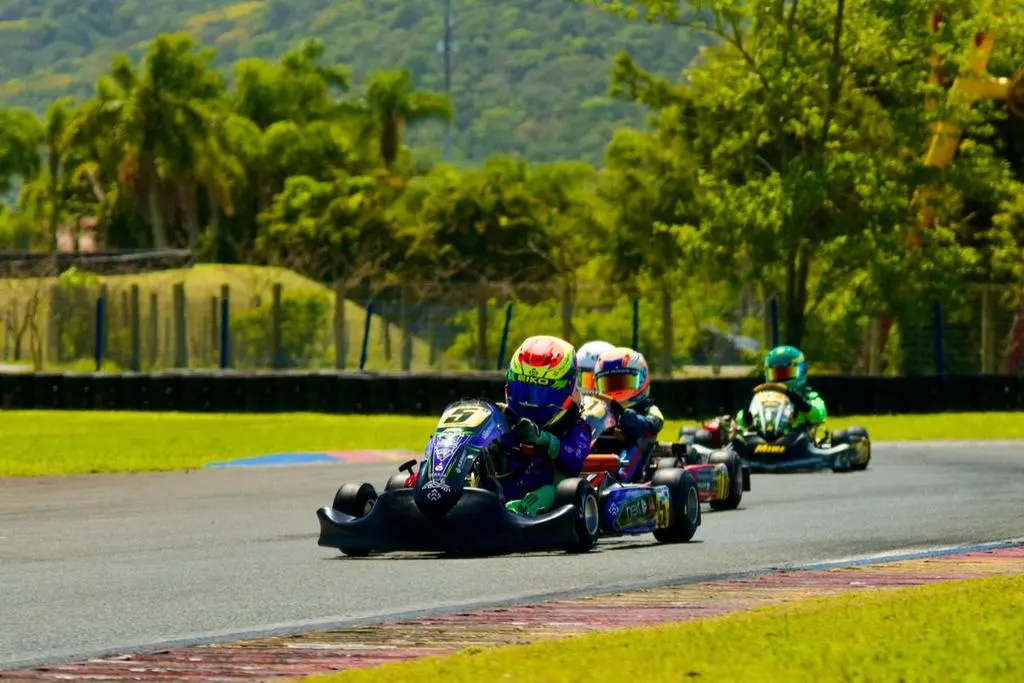Três karts em uma curva da pista do Kartódromo Beto Carrero, com palmeiras e morros ao fundo