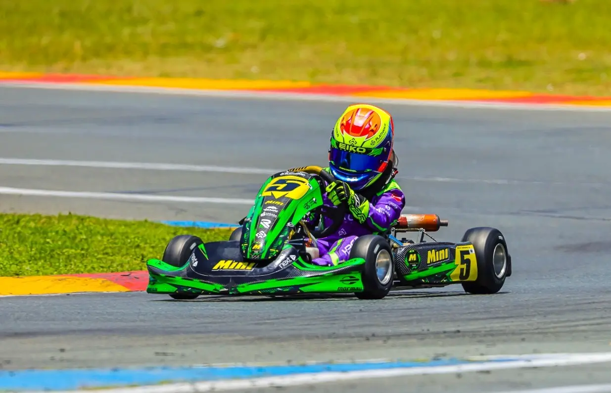 Enrico de capacete verde, laranja e azul, pilotando o kart verde número 5 em uma curva da pista