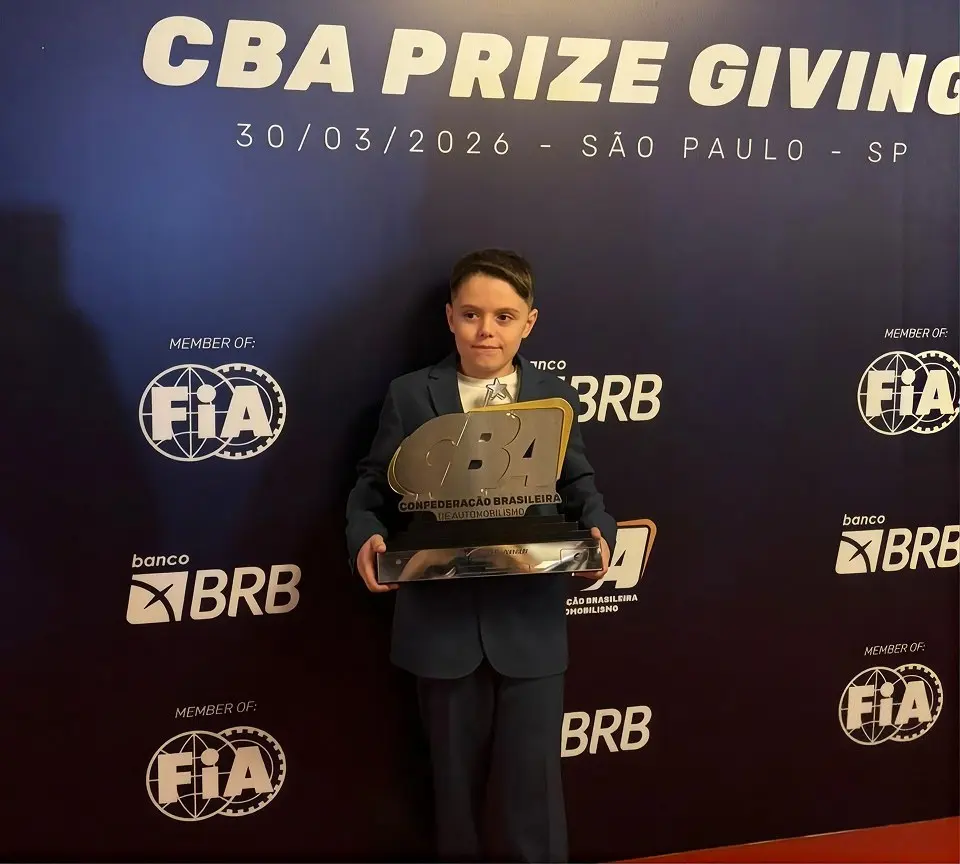 Enrico de terno, segurando o troféu da CBA, diante do painel da cerimônia de premiação da CBA em São Paulo