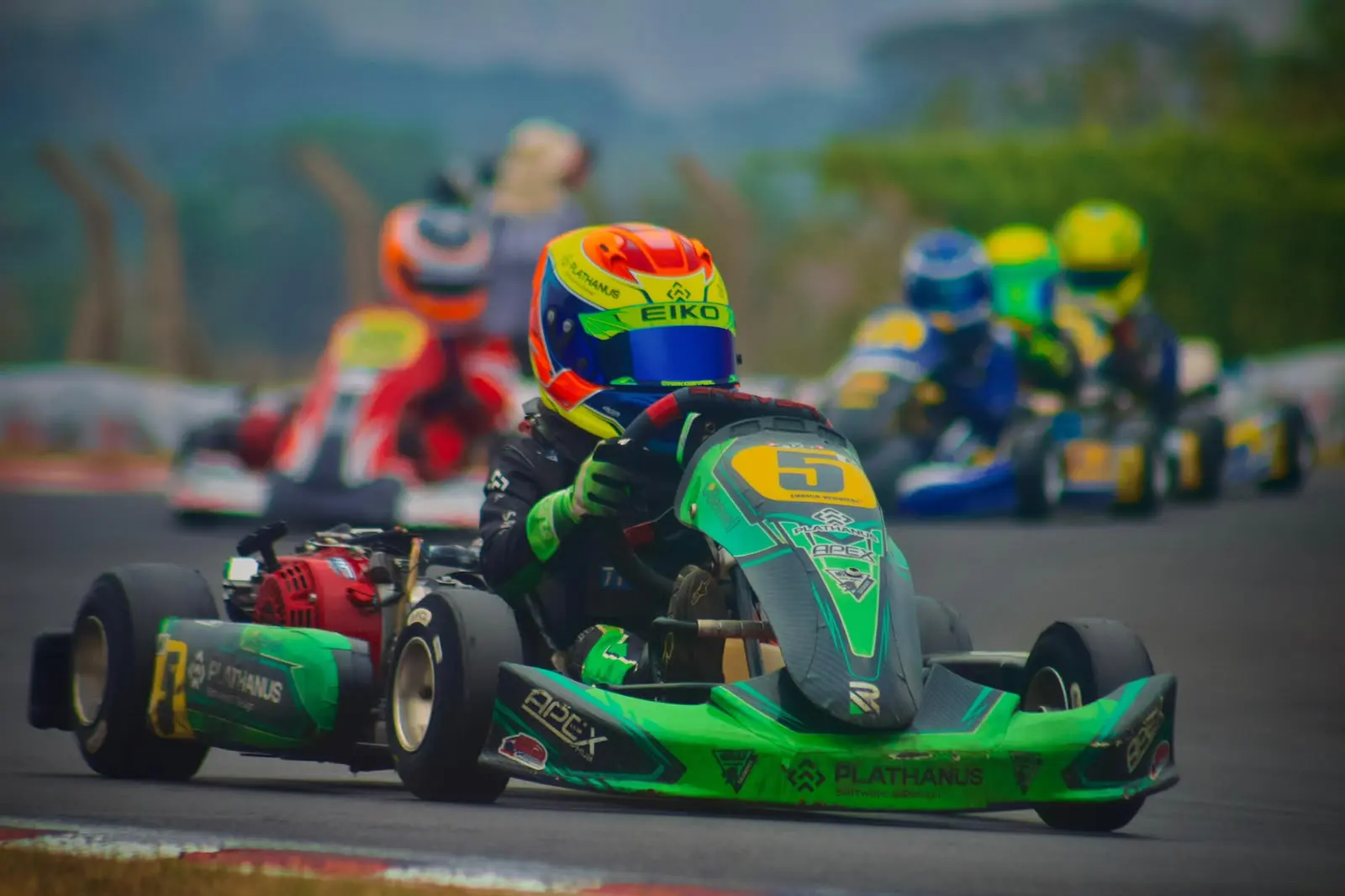Enrico, de capacete verde e laranja, pilotando o kart verde número 5, com os logos dos patrocinadores na carenagem
