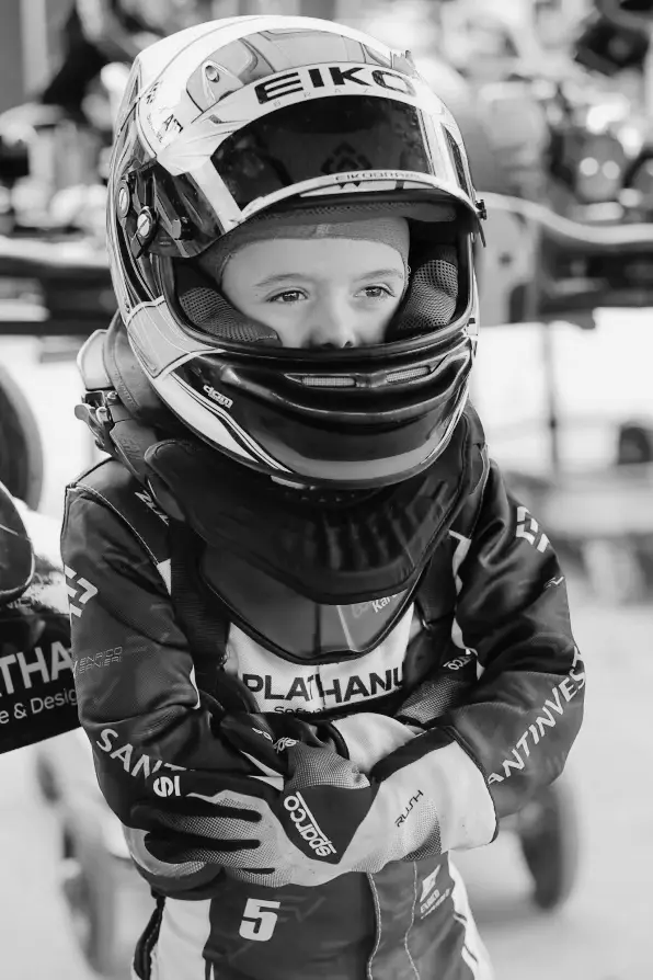Enrico de capacete e macacão de corrida, de braços cruzados e com o olhar atento, no paddock (foto em preto e branco)