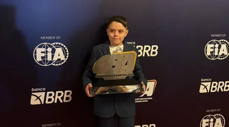 Enrico de terno, segurando o troféu da CBA, diante do painel de uma cerimônia de premiação